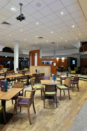 Dining area at DL Northwood Gallery with wooden tables and green-cushioned chairs under ceiling lights, and wooden accents throughout.