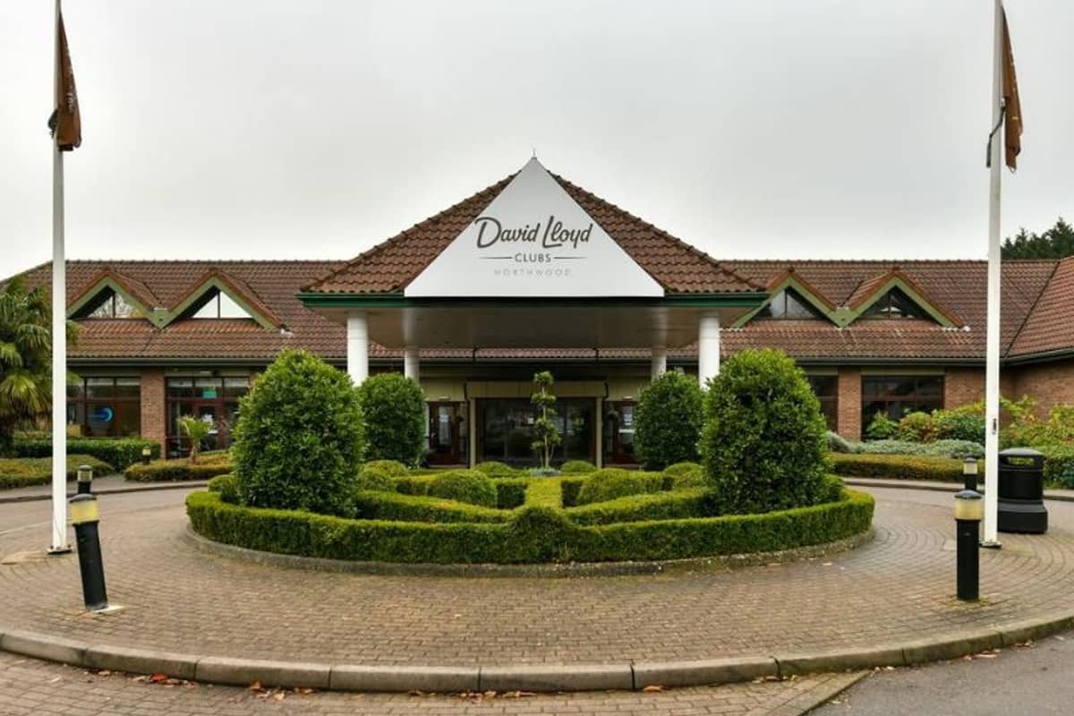 Exterior of David Lloyd Northwood Club with manicured hedges, a triangular roof, and flag poles.