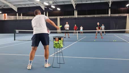 Tennis lesson at David Lloyd Southampton indoor court, featuring an instructor and adult participants practising their swings.