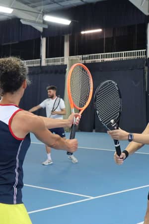 Tennis players during a training session at David Lloyd Southampton, guided by a coach on an indoor court.