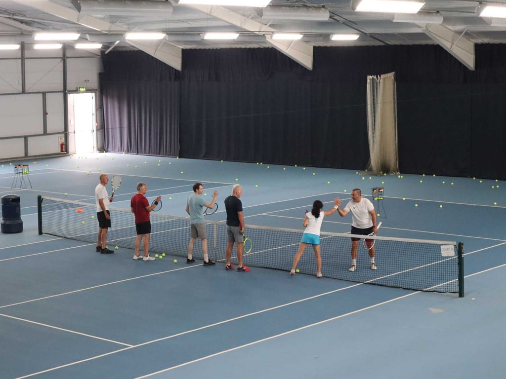 Adults playing tennis indoors at David Lloyd Southampton, engaging in a high-five over the net during a lesson.