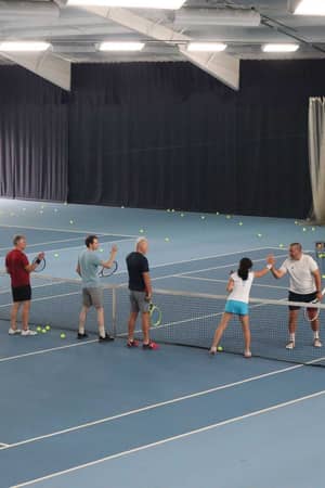 Adults playing tennis indoors at David Lloyd Southampton, engaging in a high-five over the net during a lesson.