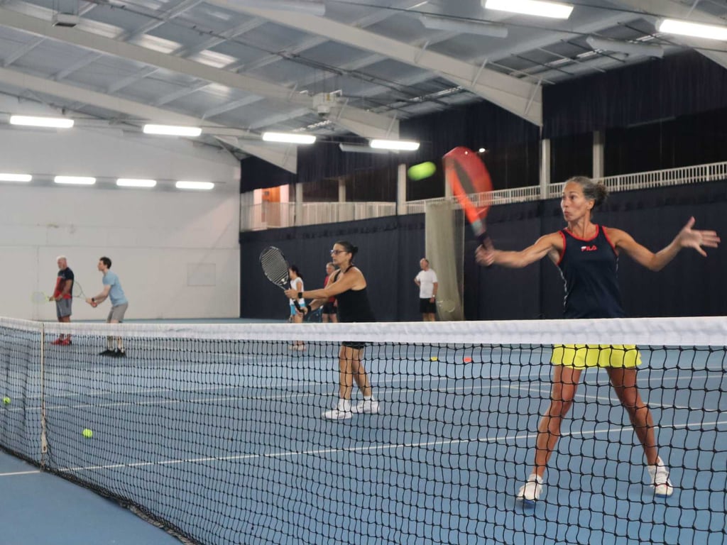 Indoor tennis court at DL Southampton with players in a doubles match, focused on hitting the ball with forehand strokes.
