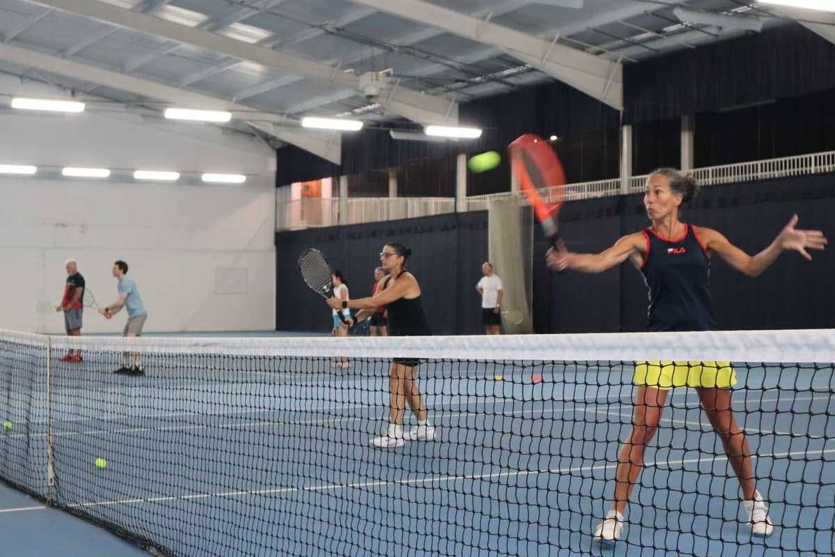 Indoor tennis court at DL Southampton with players in a doubles match, focused on hitting the ball with forehand strokes.