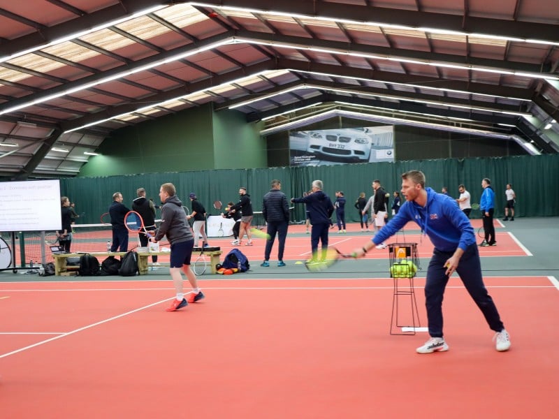 Indoor tennis coaching session with instructor guiding players on a court.