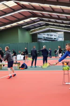 Indoor tennis coaching session with instructor guiding players on a court.
