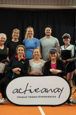 Group of tennis players on indoor court with Active Away sign, featuring nine women and one man holding tennis racquets.