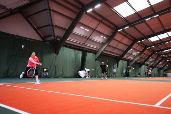 Players practising on an indoor tennis court with orange and green surfaces in West Bridgford.