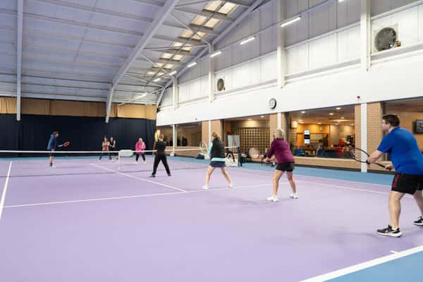 Indoor tennis facility with players engaged in a doubles match on a purple court.