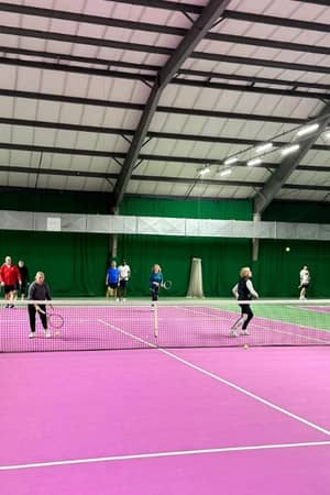 Indoor tennis court in Woking with players engaged in a doubles match on a pink surface and green walls.