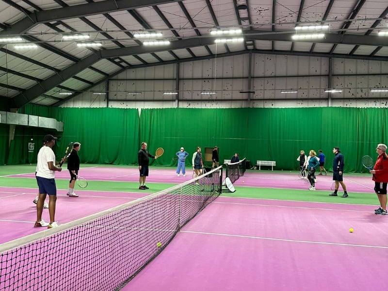 Indoor tennis coaching session with players on a pink court at DL Woking sports facility.