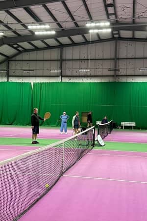 Indoor tennis coaching session with players on a pink court at DL Woking sports facility.
