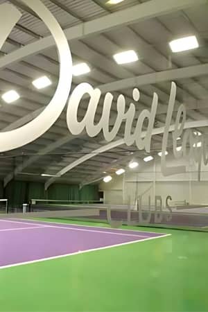 Indoor tennis court at David Lloyd Clubs, Woking, with purple and green floor and David Lloyd Clubs logo on glass window.