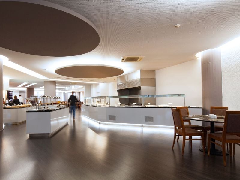 Spacious buffet area at Dom Pedro Gallery with modern design, serving stations, and wooden dining tables on polished wood flooring.