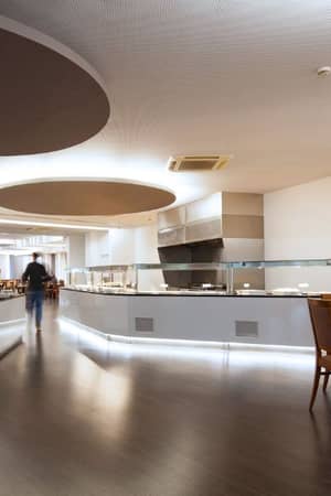 Spacious buffet area at Dom Pedro Gallery with modern design, serving stations, and wooden dining tables on polished wood flooring.