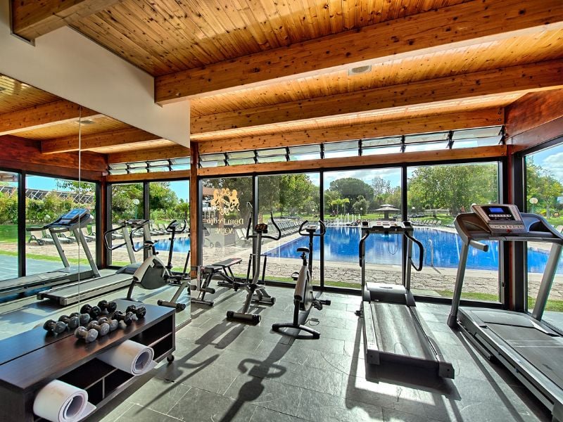 Modern gym at Dom Pedro Gallery with treadmills, bikes, and free weights, overlooking a swimming pool through large windows.