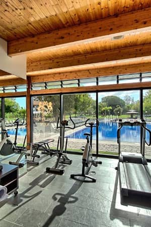 Modern gym at Dom Pedro Gallery with treadmills, bikes, and free weights, overlooking a swimming pool through large windows.