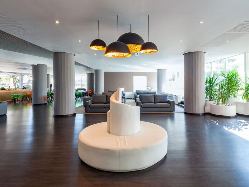 Modern lounge area in Dom Pedro Gallery with a central circular white sofa, grey armchairs, pendant lights, and potted plants.