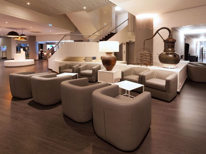 Modern lounge area with grey armchairs and white tables at Dom Pedro Gallery, featuring elegant lighting and a decorative pot.