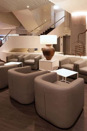 Modern lounge area with grey armchairs and white tables at Dom Pedro Gallery, featuring elegant lighting and a decorative pot.