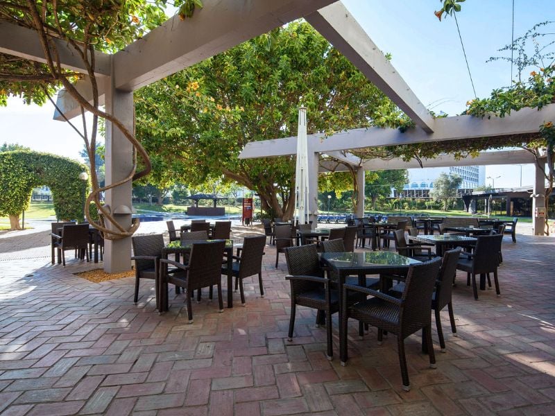 Outdoor dining area at Dom Pedro Gallery with tables and chairs under a pergola covered with greenery, surrounded by garden views.