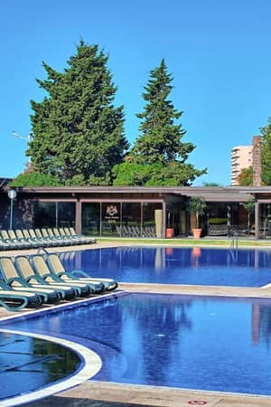 Dom Pedro Gallery pool lounge with a clear blue pool, sun loungers, and surrounding trees under a blue sky.