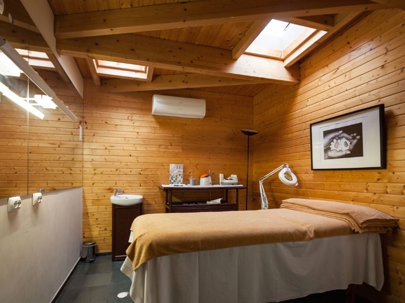 Spa treatment room at Dom Pedro Gallery with wooden walls, skylights, a massage table, and wellness products.