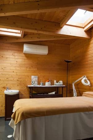 Spa treatment room at Dom Pedro Gallery with wooden walls, skylights, a massage table, and wellness products.