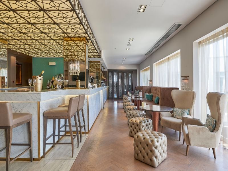 Elegant bar at Dona Filipa Hotel with a marble counter, gold accents, plush seating, and geometric ceiling lights.
