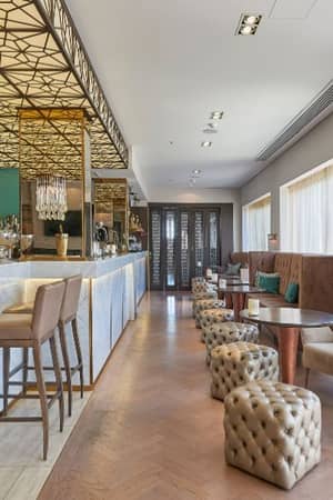 Elegant bar at Dona Filipa Hotel with a marble counter, gold accents, plush seating, and geometric ceiling lights.