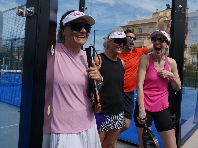 Group of four friends laughing and holding padel rackets at Dona Filipa Padel court, dressed in sportswear with visors and sunglasses.