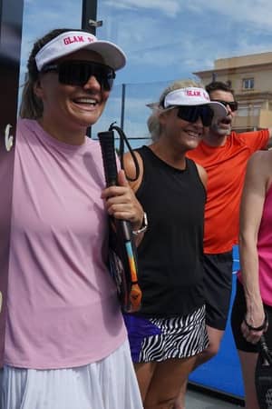 Group of four friends laughing and holding padel rackets at Dona Filipa Padel court, dressed in sportswear with visors and sunglasses.