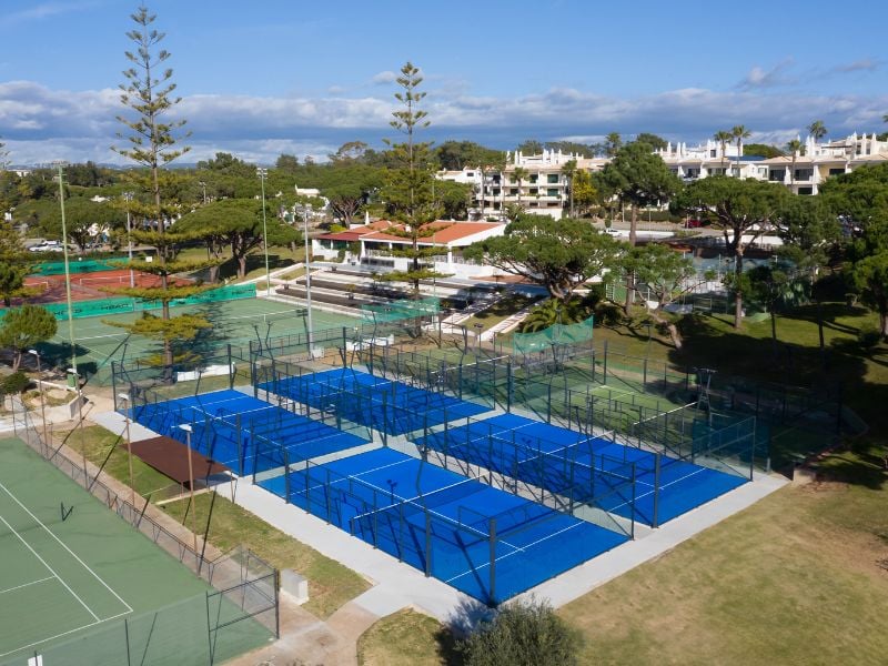 Aerial view of blue padel courts at Dona Filipa, surrounded by green areas and neighbouring tennis courts.