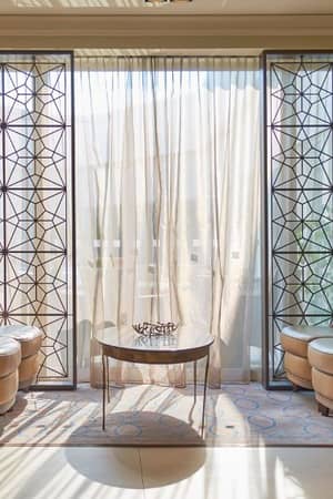 Lounge area at Dona Filipa Hotel with beige armchairs, blue cushions, a glass coffee table, and geometric-patterned screens.