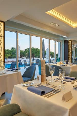 Interior of the Dona Filipa Hotel restaurant with tables set for fine dining, overlooking the pool and lush greenery through expansive windows.