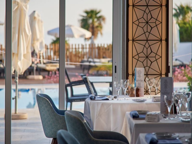 Dining tables with white tablecloths and fine glassware, set by the pool at Dona Filipa Hotel, with outdoor seating and sun loungers in view.