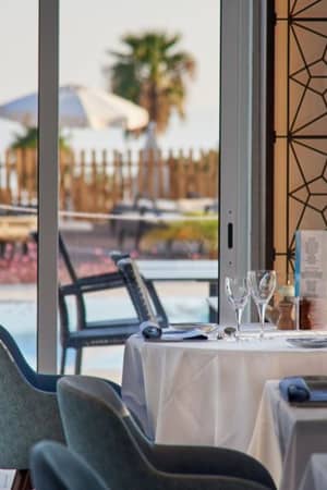 Dining tables with white tablecloths and fine glassware, set by the pool at Dona Filipa Hotel, with outdoor seating and sun loungers in view.