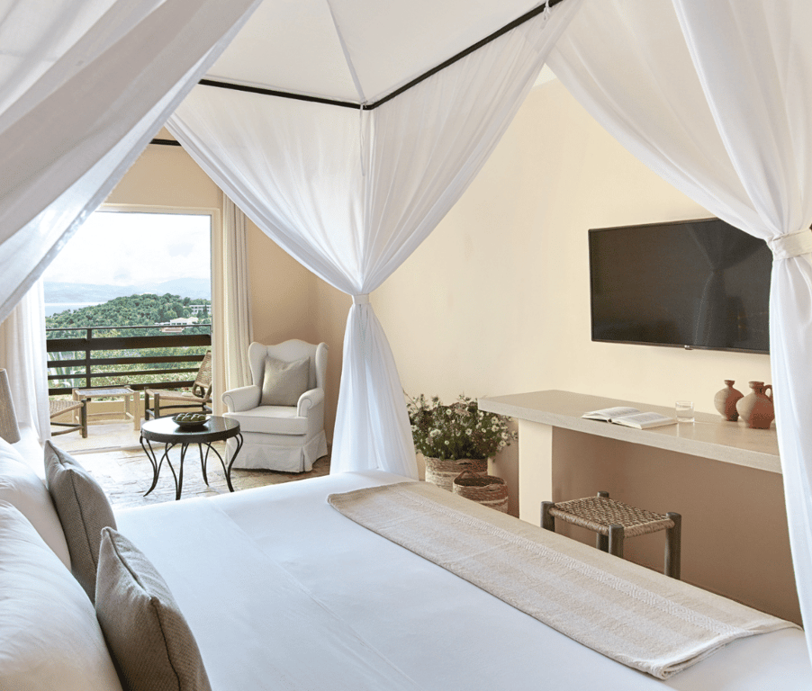 Luxurious bungalow interior at Daphnila Bay with a canopy bed, TV, and balcony overlooking greenery.