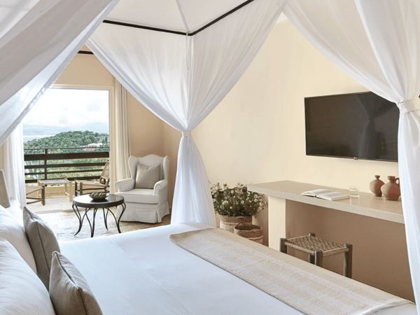 Luxurious bungalow interior at Daphnila Bay with a canopy bed, TV, and balcony overlooking greenery.