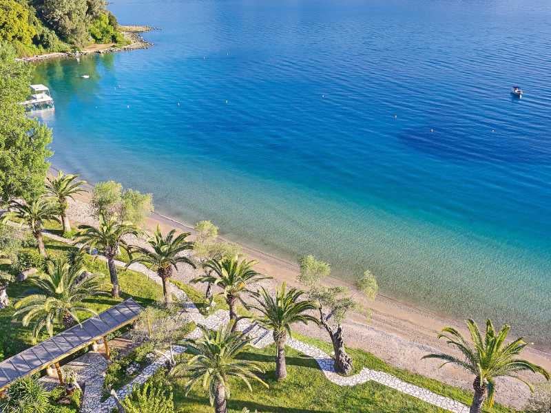 Aerial view of Daphnila Bay featuring a beachfront with palm trees and clear turquoise waters, with a docked boat visible.
