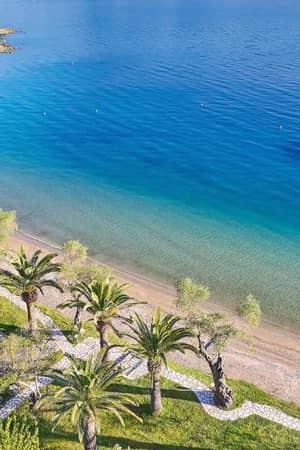 Aerial view of Daphnila Bay featuring a beachfront with palm trees and clear turquoise waters, with a docked boat visible.