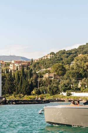 View of a cruise in Daphnila Bay with a backdrop of green hills, buildings, and a white chapel by the water.