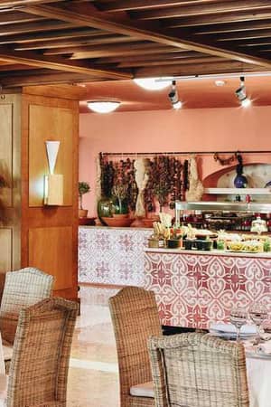 Indoor view of Daphnila Bay restaurant, with round tables, wicker chairs, and a buffet station in a warmly decorated setting.
