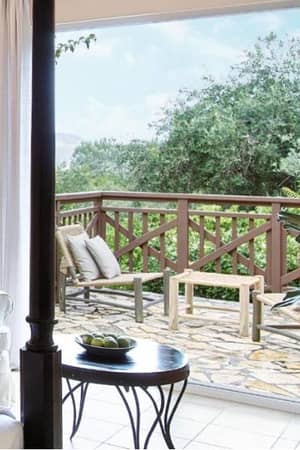 Balcony view from a room at Daphnila Bay, with a white armchair, round table, and lush greenery outside.