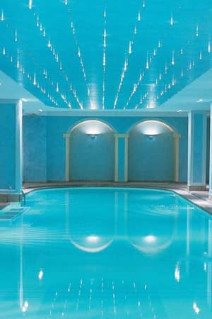 Indoor swimming pool at Daphnila Bay spa with blue walls, ceiling lights, and entry steps.