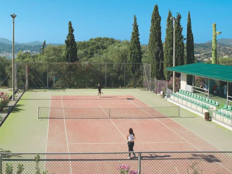 Tennis courts at Daphnila Bay with players, surrounded by greenery, cypress trees, and hills in the background.