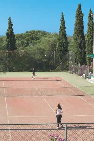 Tennis courts at Daphnila Bay with players, surrounded by greenery, cypress trees, and hills in the background.