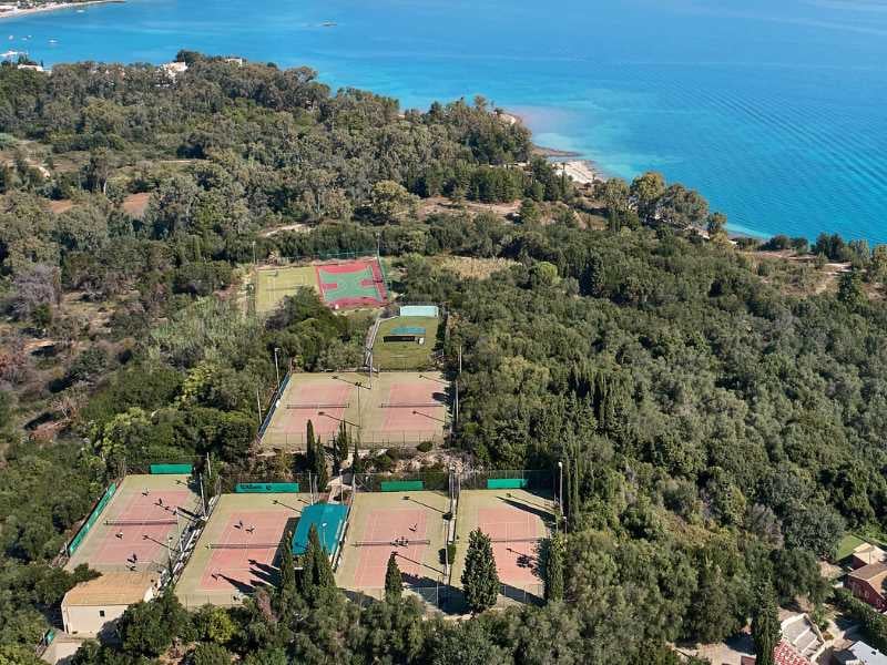 Aerial view of tennis courts surrounded by greenery near the waters of Daphnila Bay.