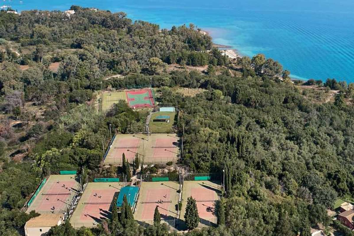 Aerial view of tennis courts surrounded by greenery near the waters of Daphnila Bay.