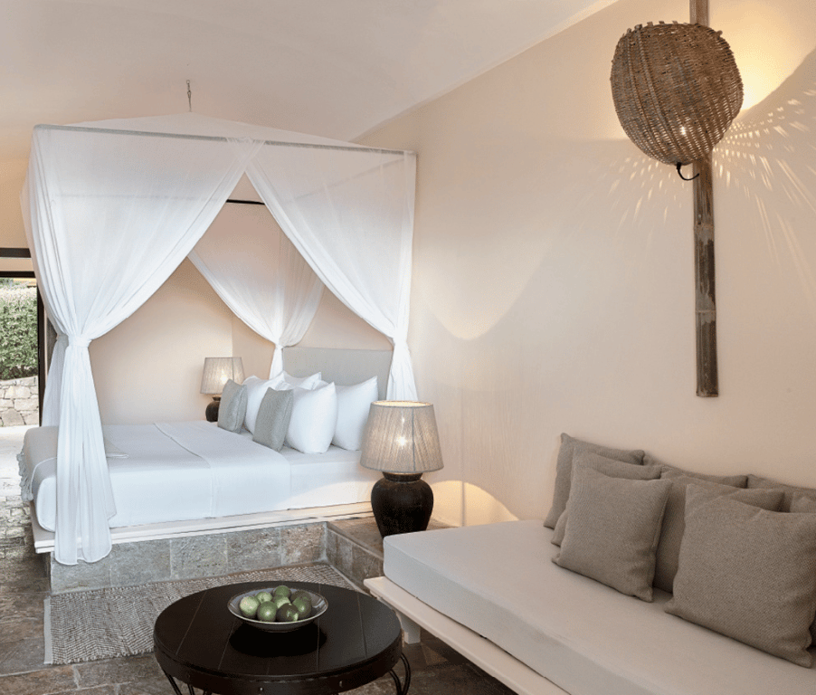 Interior of a Daphnila Bay Hideaway Bungalow with a four-poster bed, seating area, and ambient lighting, featuring a touch of luxury with a limited sea view.